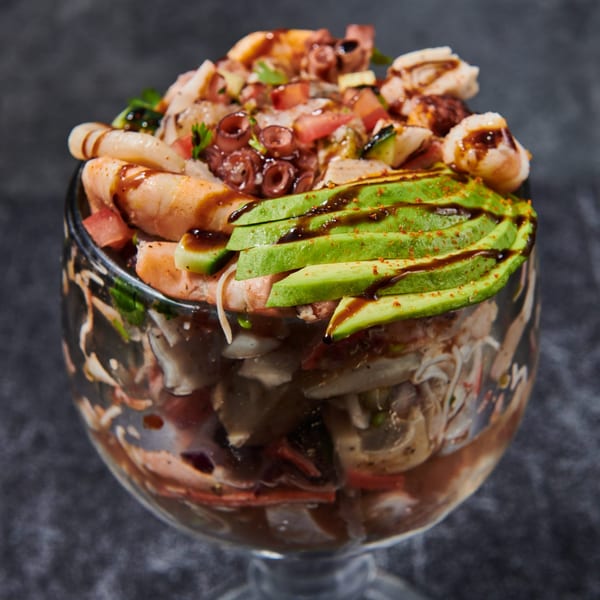 A large glass of El Sushi Loco's seafood cocktail, topped with avocado slices and dark sauce.