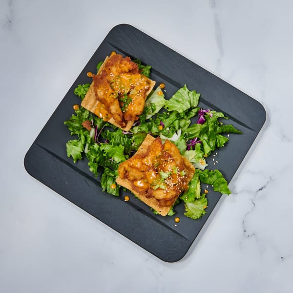 Two crispy shrimp wontons with sauce, sesame seeds, and green onions, served on a bed of lettuce.