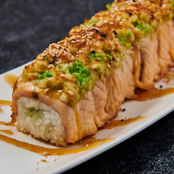 El Sushi Loco's baked salmon roll with avocado, sesame seeds, and sauce on a white plate.