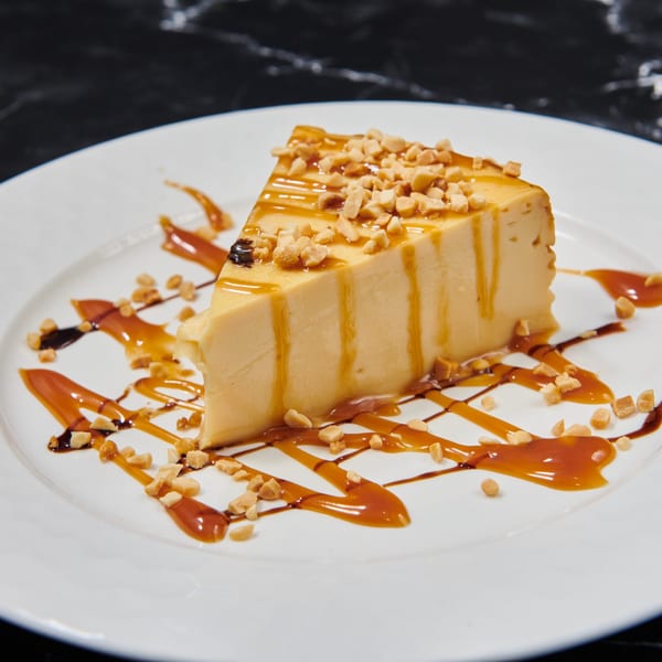 Slice of flan with caramel drizzle and chopped nuts on a white plate.