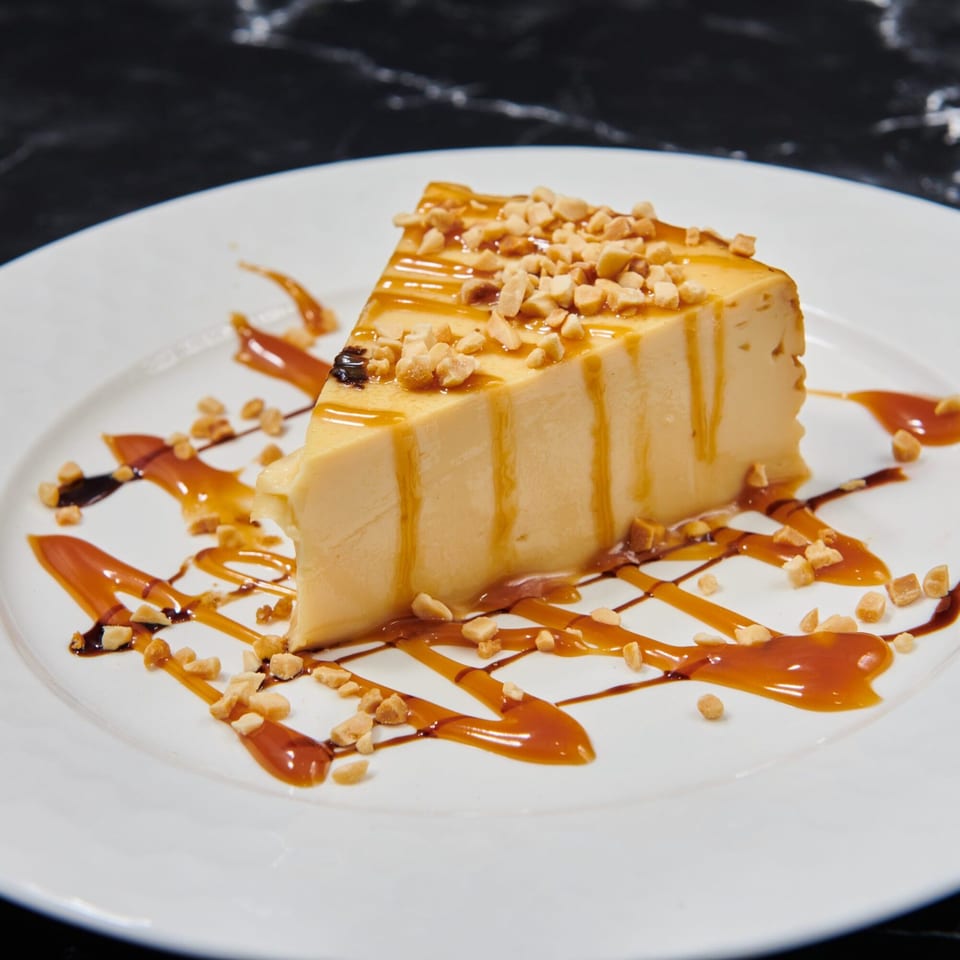 Slice of flan with caramel drizzle and chopped nuts on a white plate.