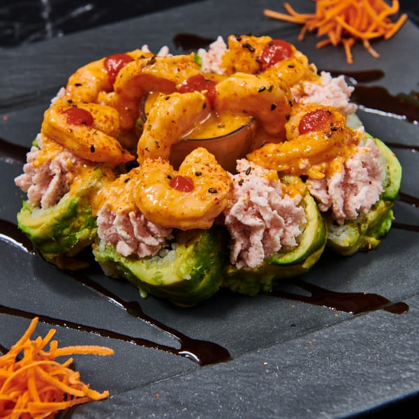 El Sushi Loco's sushi roll with avocado, crab, shrimp, and spicy sauce on a dark plate.