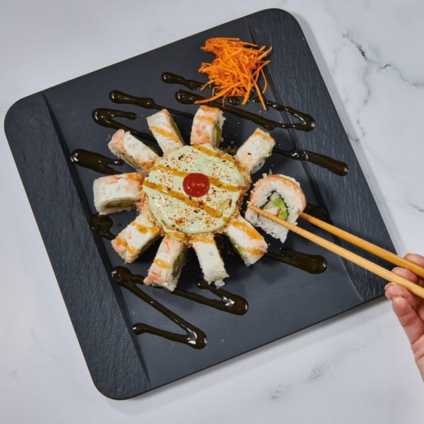 El Sushi Loco's sushi rolls arranged in a circle with a creamy sauce, garnished with shredded carrots.