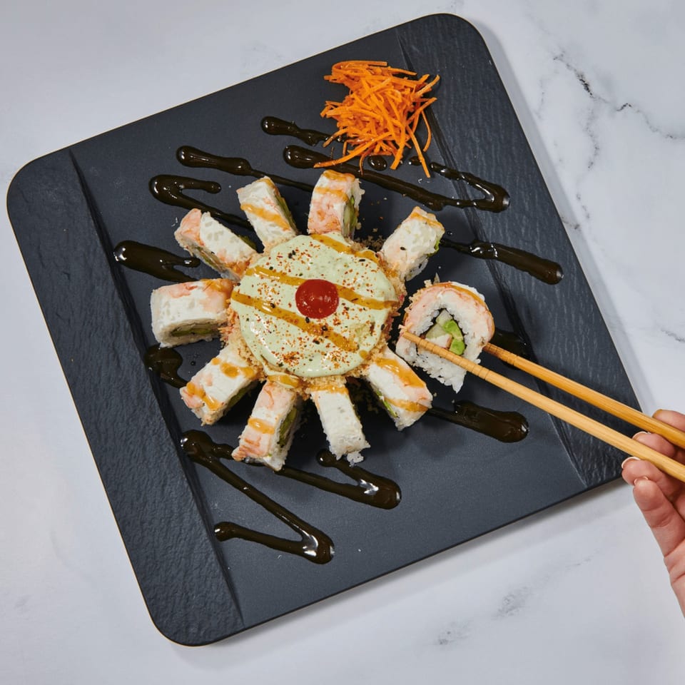 El Sushi Loco's sushi rolls arranged in a circle with a creamy sauce, garnished with shredded carrots.