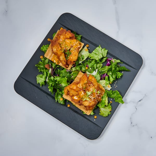 Two crispy shrimp wontons with sauce, sesame seeds, and green onions on a bed of mixed greens.