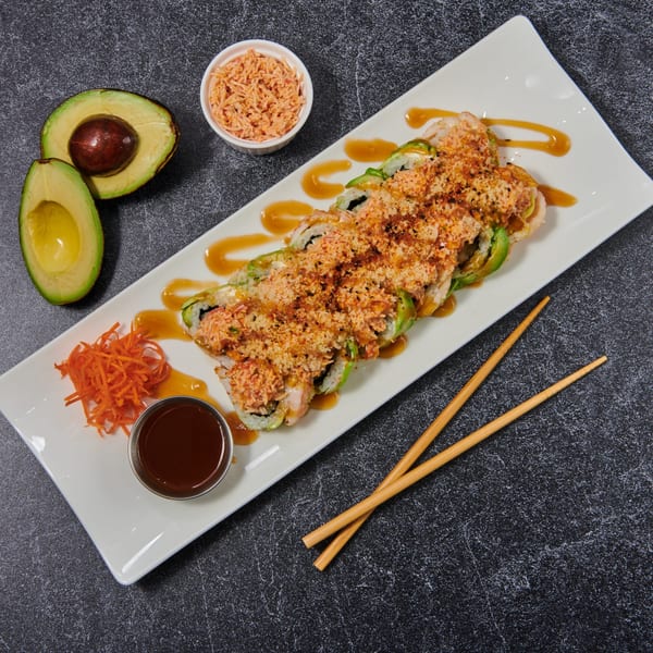 El Sushi Loco sushi roll with avocado, sauce, shredded carrots, and chopsticks on a white plate.