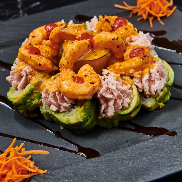 El Sushi Loco's sushi roll with shrimp, avocado, and a creamy sauce on a dark plate.
