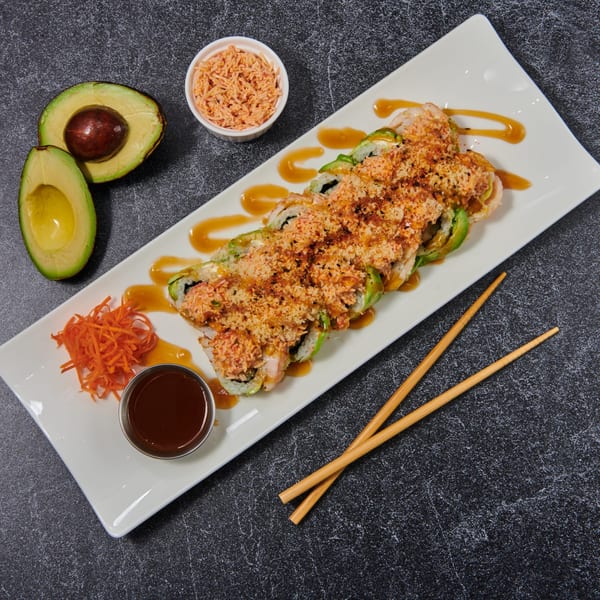 El Sushi Loco's sushi roll topped with avocado, sauce, and crispy bits, with avocado halves and chopsticks.