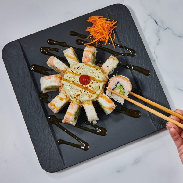 El Sushi Loco's sushi rolls arranged around a creamy sauce, with chopsticks picking up a piece.