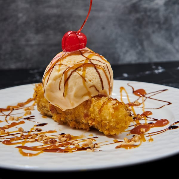 Fried banana dessert with a scoop of ice cream, caramel, chocolate drizzle, and a cherry.