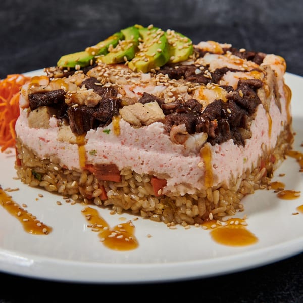El Sushi Loco's sushi cake with rice, pink filling, meat, avocado, sesame seeds, and sauce.