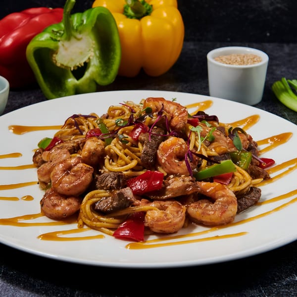 El Sushi Loco's shrimp and beef stir-fry noodles with bell peppers and sauce on a white plate.
